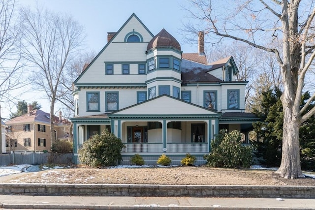 victorian-style house featuring covered porch, a chimney, and fence