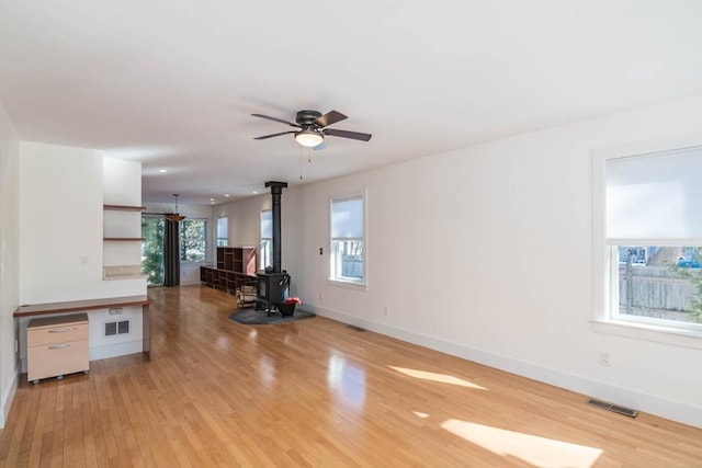 unfurnished living room with a wood stove, light wood-style flooring, visible vents, and baseboards