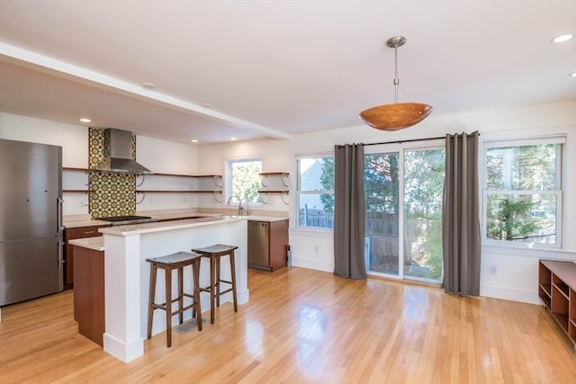 kitchen featuring open shelves, light countertops, appliances with stainless steel finishes, light wood-style floors, and wall chimney range hood