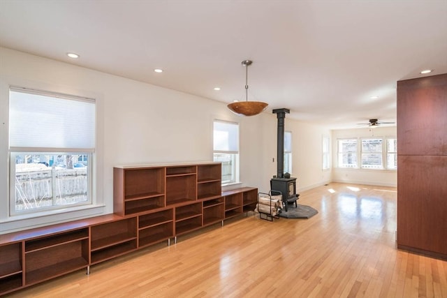 living area featuring baseboards, a ceiling fan, a wood stove, light wood-style floors, and recessed lighting