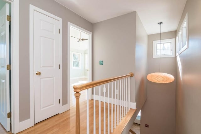 hallway with light wood-type flooring, baseboards, and an upstairs landing