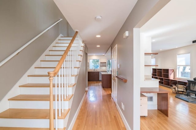 staircase featuring recessed lighting, a wood stove, baseboards, and wood finished floors