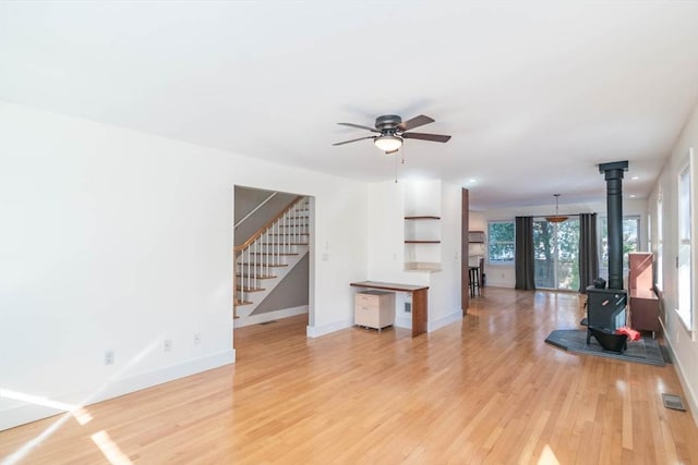 unfurnished living room with light wood-style flooring, visible vents, baseboards, stairway, and a wood stove