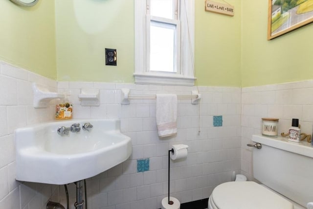 half bath with wainscoting, toilet, tile walls, and a sink