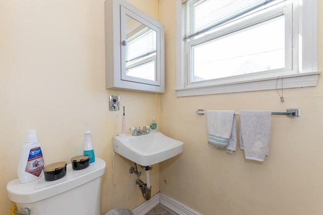 half bath with toilet, baseboards, and a sink