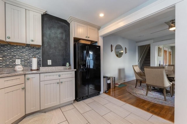 kitchen featuring light stone counters, wood finish floors, ceiling fan, backsplash, and black fridge