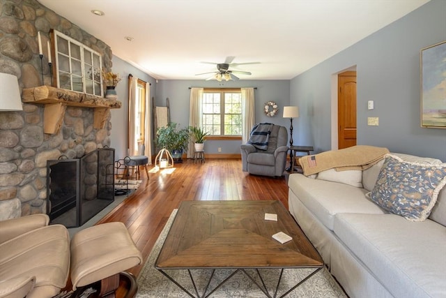 living area with wood-type flooring, a ceiling fan, baseboards, and a stone fireplace