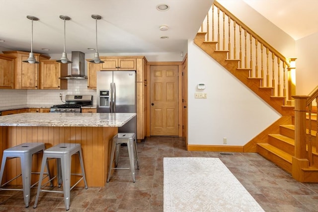 kitchen with decorative backsplash, a breakfast bar area, wall chimney exhaust hood, appliances with stainless steel finishes, and hanging light fixtures