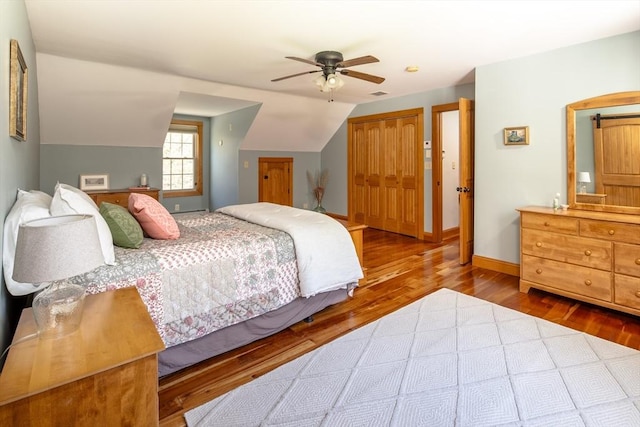 bedroom with a closet, lofted ceiling, wood finished floors, baseboards, and a ceiling fan