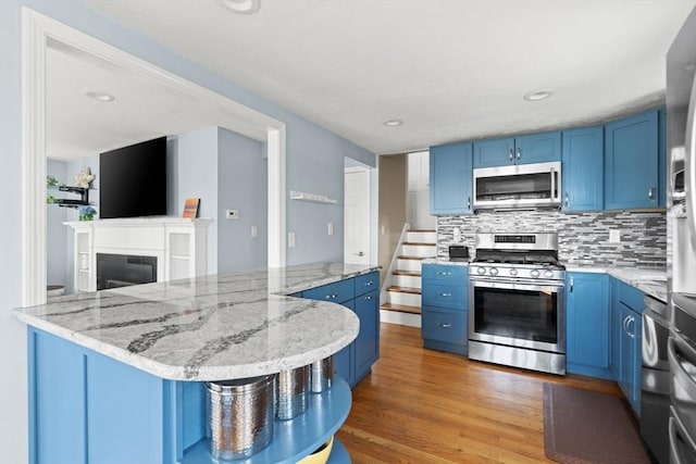 70 Williams St, Quincy, MA 02171 - kitchen with stainless steel appliances, blue cabinets, light wood-type flooring, tasteful backsplash, and light stone counters