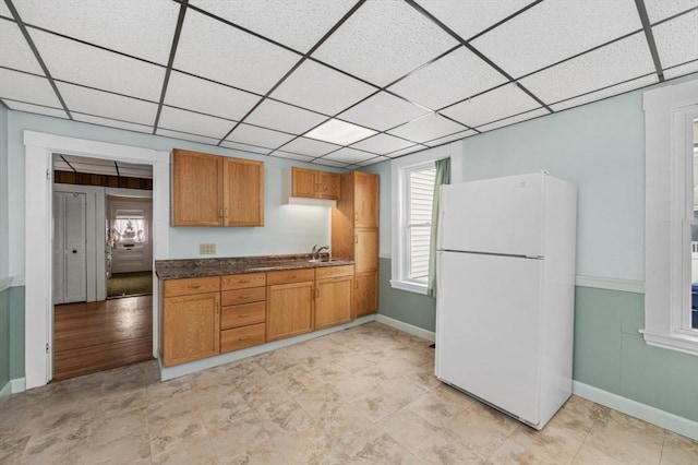 kitchen featuring dark countertops, a drop ceiling, a sink, and freestanding refrigerator