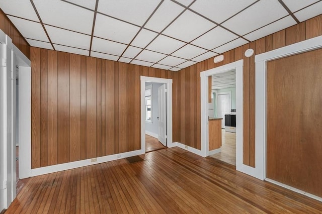 unfurnished room featuring wood walls, wood-type flooring, a paneled ceiling, and baseboards