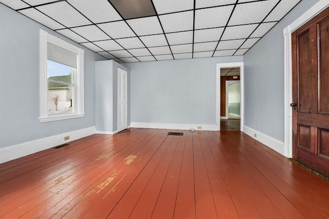 empty room with a drop ceiling, hardwood / wood-style flooring, and baseboards