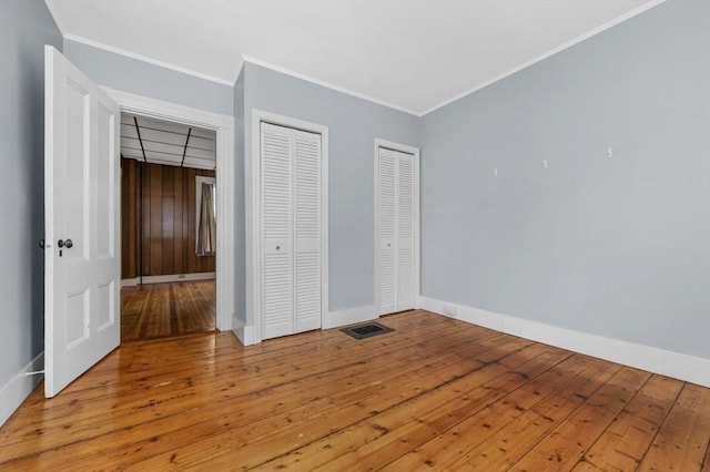 unfurnished bedroom with crown molding, hardwood / wood-style floors, visible vents, and baseboards