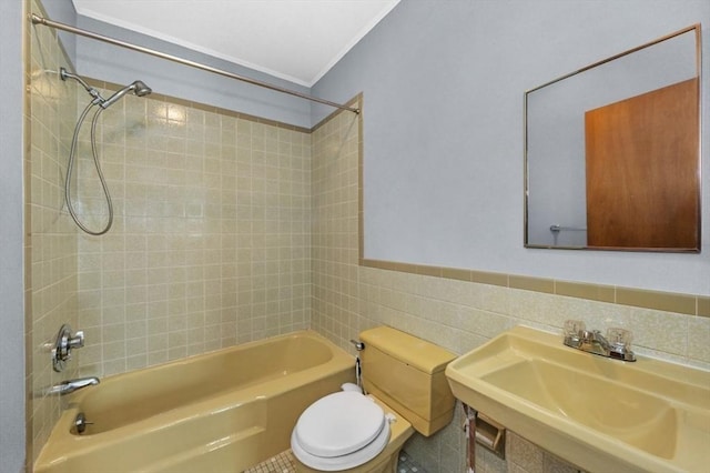 bathroom featuring bathtub / shower combination, toilet, a sink, tile walls, and wainscoting