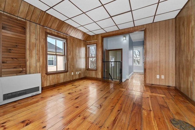 empty room featuring baseboards, light wood finished floors, wood walls, and heating unit