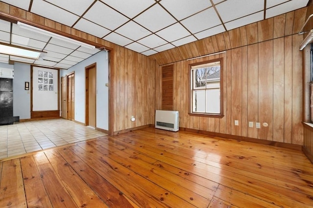 empty room with wood-type flooring, a drop ceiling, wood walls, and heating unit