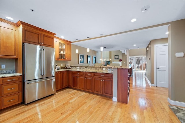 kitchen featuring glass insert cabinets, light wood-type flooring, a peninsula, high quality fridge, and brown cabinetry