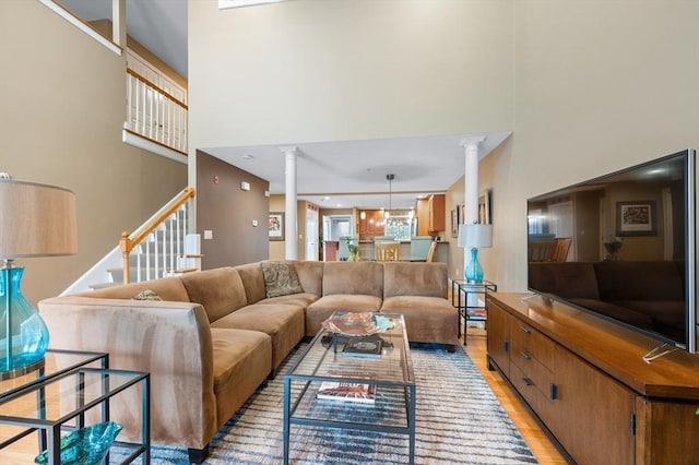 living area featuring stairs, decorative columns, light wood-style floors, and a towering ceiling