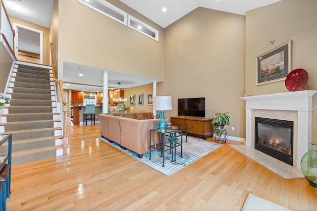 living area featuring a high end fireplace, stairs, wood-type flooring, and decorative columns