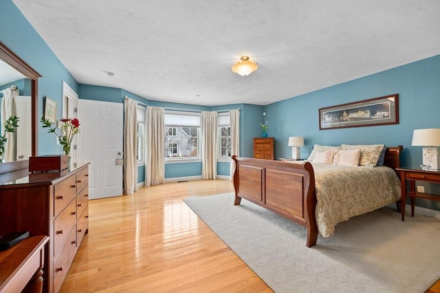 bedroom featuring light wood-style flooring, a textured ceiling, and baseboards