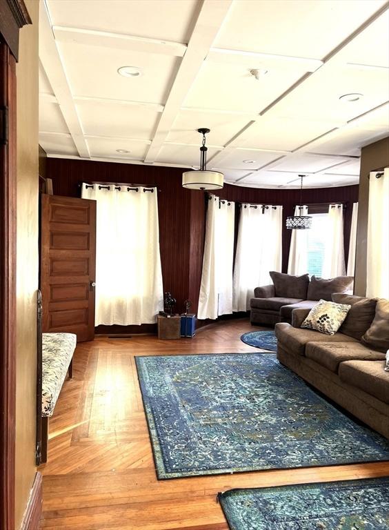 living area featuring coffered ceiling, wood walls, and wood finished floors