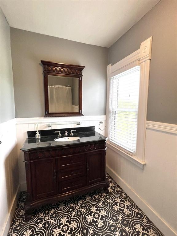 bathroom with a wainscoted wall, tile patterned flooring, vanity, and baseboards