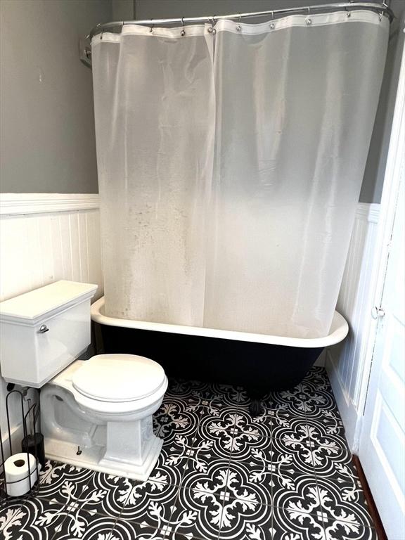 bathroom with toilet, a wainscoted wall, tile patterned flooring, and shower / bath combo with shower curtain