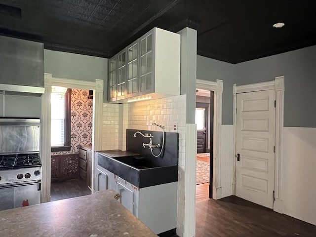 kitchen featuring a sink, stainless steel gas range, dark wood-style floors, tasteful backsplash, and glass insert cabinets