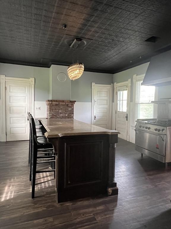 kitchen featuring dark wood finished floors, wainscoting, gas range, an ornate ceiling, and wall chimney range hood