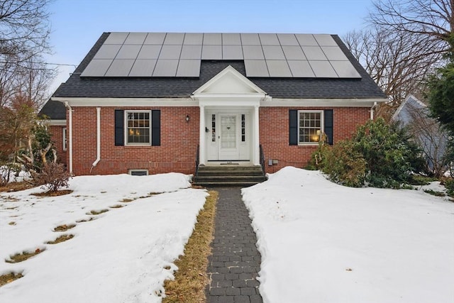 view of front of property with solar panels, brick siding, and roof with shingles