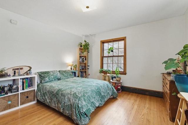 bedroom featuring light wood finished floors, baseboards, and a baseboard heating unit