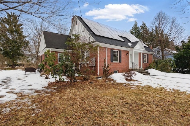 snow covered property featuring solar panels and brick siding