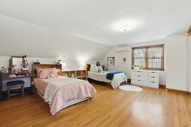 bedroom featuring light wood-style floors, baseboards, vaulted ceiling, and a wall mounted air conditioner