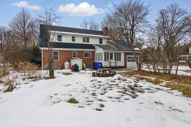 snow covered house featuring brick siding, a chimney, and an attached garage