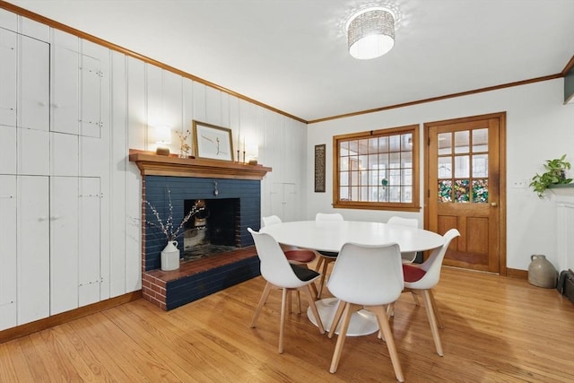 dining area featuring light wood-style flooring, a fireplace, ornamental molding, and baseboards