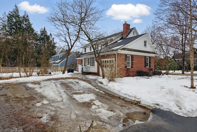 view of snow covered exterior featuring a garage, brick siding, and a chimney