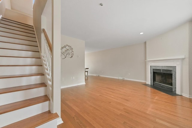 unfurnished living room with recessed lighting, stairway, light wood-style floors, a fireplace with flush hearth, and baseboards