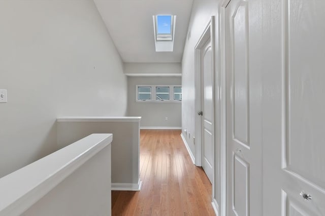 corridor featuring light wood-style floors, a skylight, baseboards, and an upstairs landing