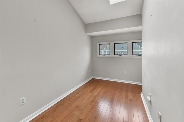 unfurnished room with a skylight, wood-type flooring, and baseboards