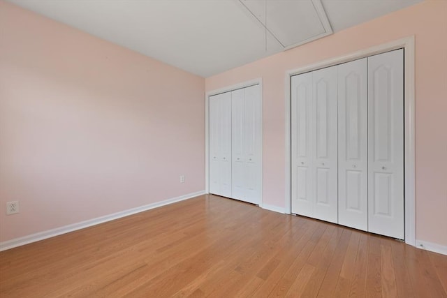 unfurnished bedroom with light wood-style flooring, attic access, baseboards, and two closets