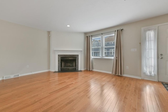 unfurnished living room with light wood finished floors, a fireplace with flush hearth, visible vents, and baseboards