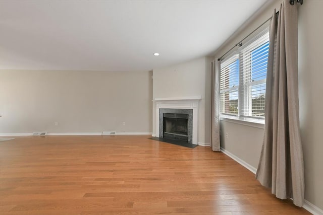 unfurnished living room with recessed lighting, a fireplace with flush hearth, visible vents, baseboards, and light wood finished floors