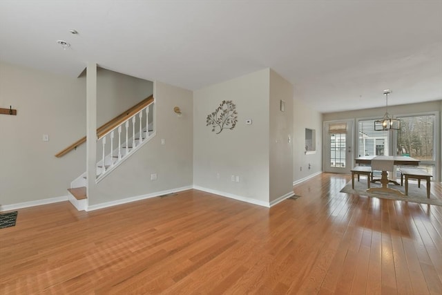 living area featuring visible vents, baseboards, stairs, light wood-style floors, and an inviting chandelier