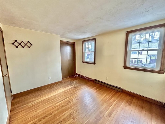 empty room featuring baseboard heating, a textured ceiling, and light wood-type flooring