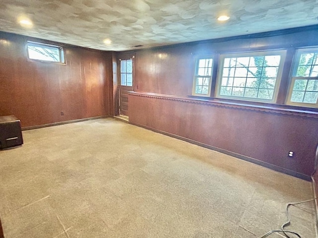 basement with light carpet, a healthy amount of sunlight, and wooden walls