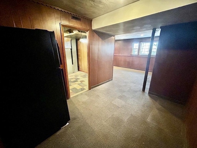 basement with wooden walls and black fridge