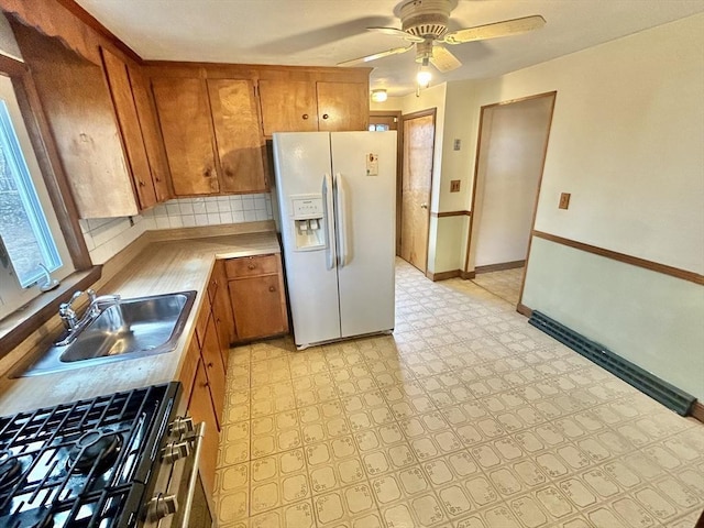 kitchen with ceiling fan, decorative backsplash, gas range, white refrigerator with ice dispenser, and sink