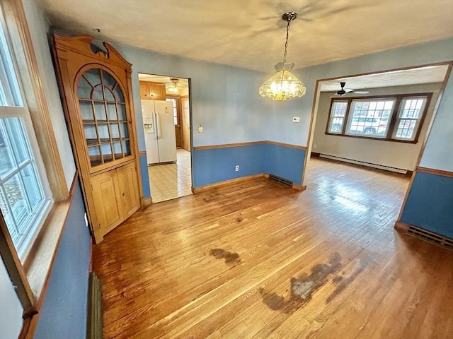 unfurnished dining area with ceiling fan with notable chandelier, wood-type flooring, and a baseboard heating unit