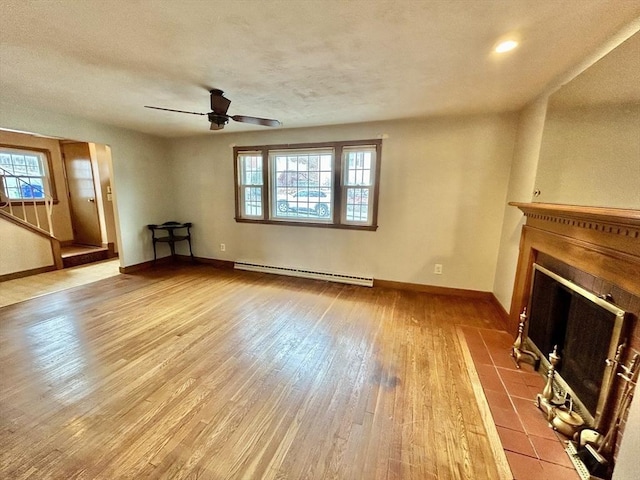 unfurnished living room with baseboard heating, light hardwood / wood-style floors, a tile fireplace, and ceiling fan